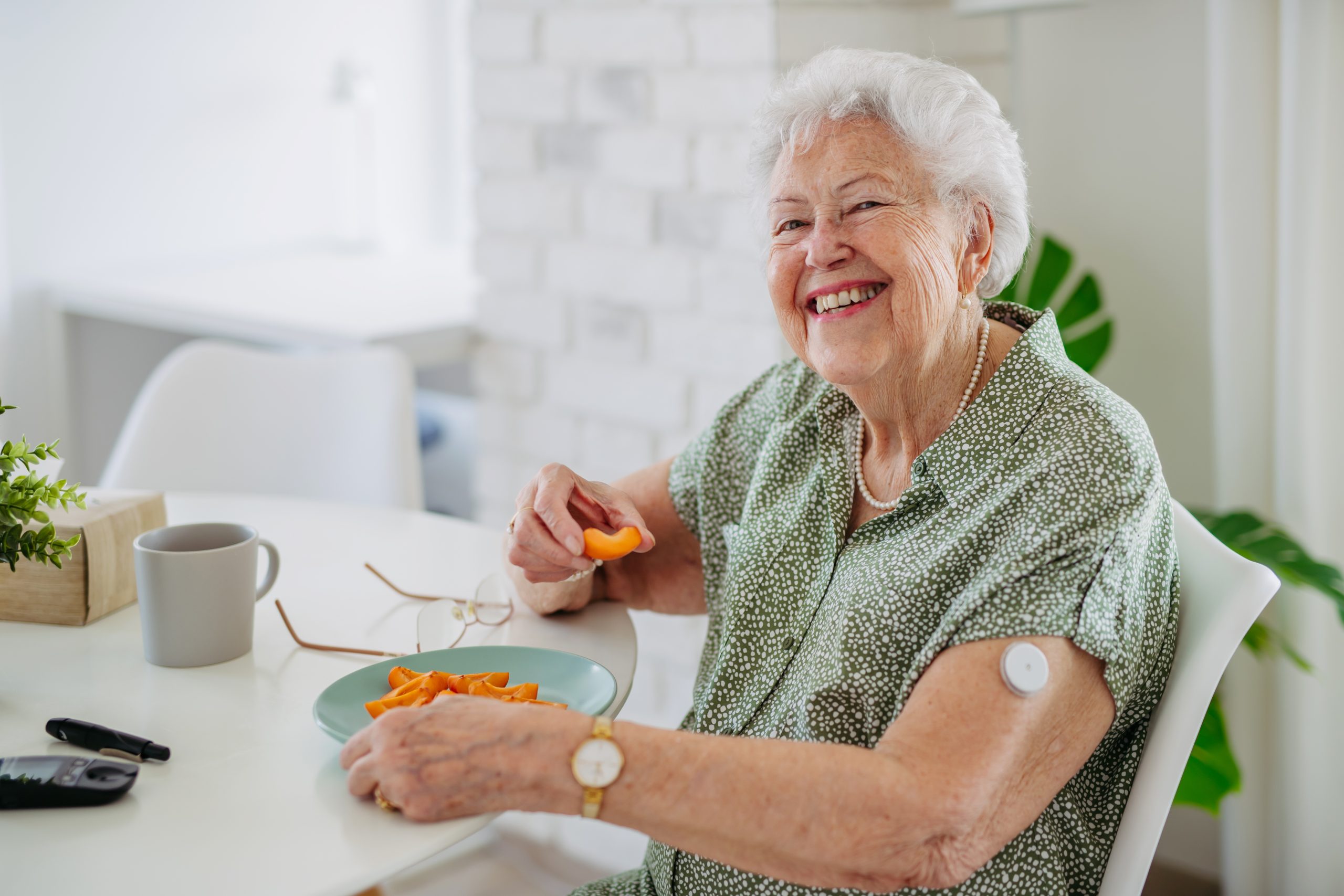 Starija žena dijabetičar jede voće za stolom i smeje se